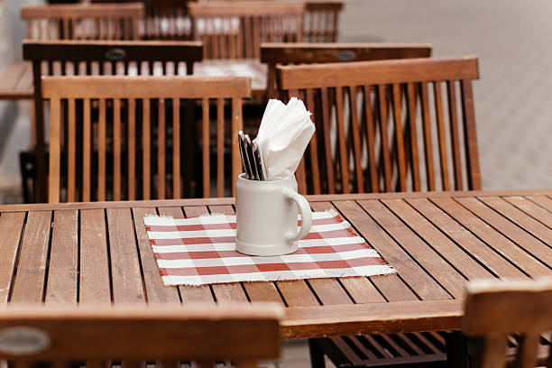 istock A charming rustic outdoor dining setup featuring a wooden table with a checkered placemat, a ceramic mug holding napkins and cutlery, creating a cozy and inviting atmosphere perfect for al fresco dining. 2208135658