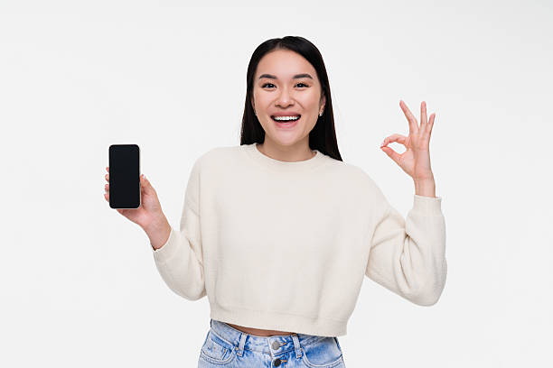 istock Young Woman Smiling and Gesturing OK Sign While Holding a Smartphone 2208135839