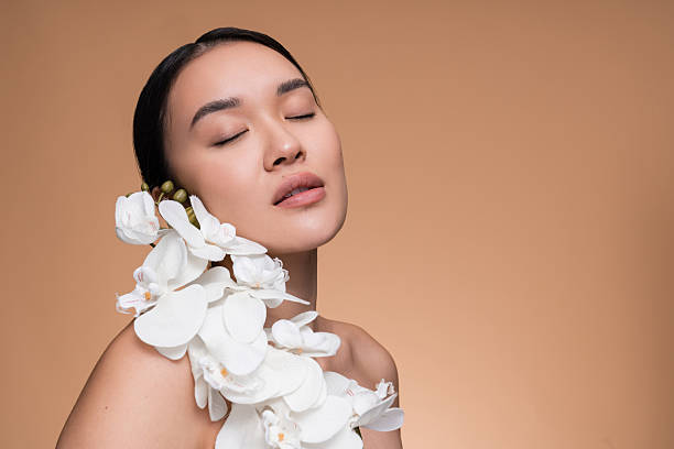 Elegant portrait of a woman surrounded by white orchids, radiating peace and natural beauty, against a neutral backdrop. Perfect for concepts of simplicity, beauty, nature, wellness, and inner peace.