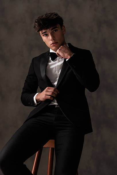 istock elegant young man in black tuxedo adjusting bowtie and posing 2208151321