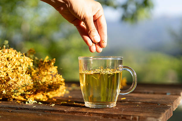 istock Hand adding herbs to a cup of tea beside St. John's wort flower 2208152302
