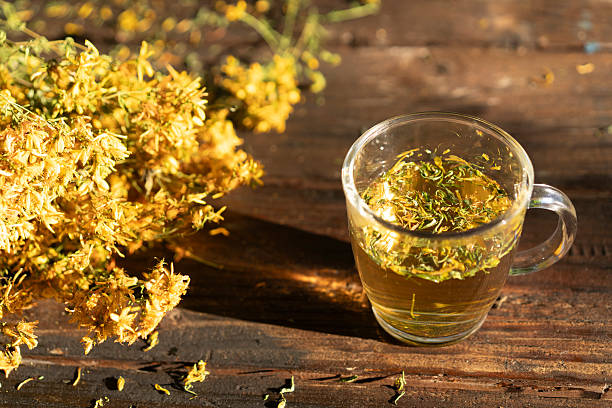 A beautifully arranged scene featuring a glass of herbal tea surrounded by vibrant golden flowers, embodying a sense of tranquility and natural elegance.