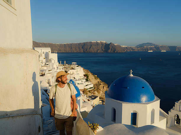 Serene man walking on Santorini island looking at seaside at sunset  during experiential island hopping trip in Greece