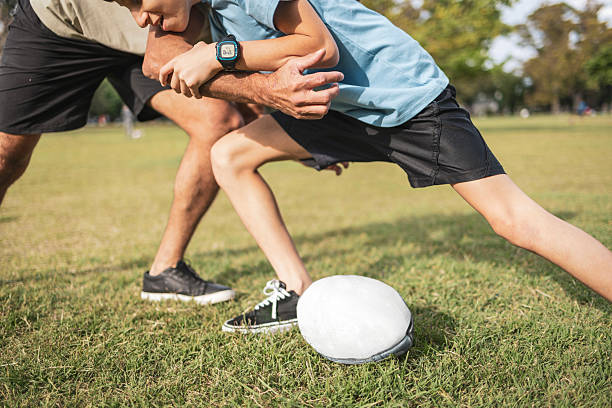 A bonding moment featuring a father playing rugby with his son outdoors on a sunny park field. Promotes family connection, outdoor activity, and physical fitness.