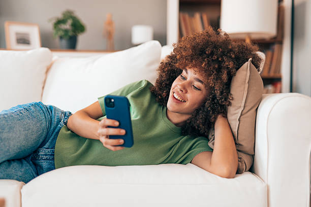 istock Young woman lying on sofa using mobile phone at home 2208167356