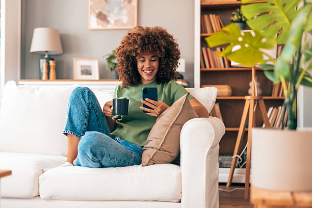 istock Young woman relaxing on the sofa, drinking coffee and using smartphone 2208167376