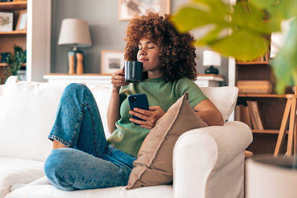 istock Young woman relaxing on the sofa, drinking coffee and using her smartphone 2208167378