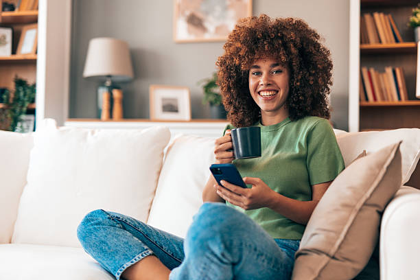 istock Young woman relaxing on the sofa, drinking coffee and using smartphone 2208167408