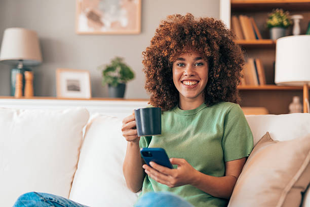 istock Young woman relaxing on the sofa, drinking coffee and using her phone 2208167411