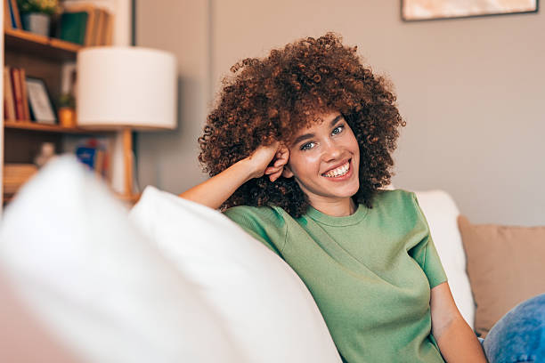 istock Young woman relaxing on sofa smiling at camera 2208167414