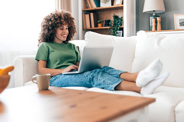 istock Young woman relaxing on the sofa and working on her laptop 2208167524
