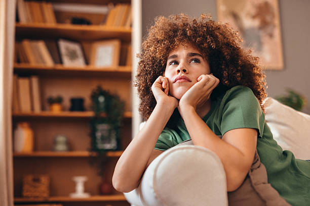 istock Young woman relaxing on sofa and looking up, thinking about something 2208167574