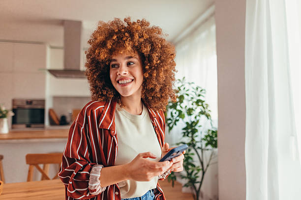 istock Young woman using mobile phone, smiling and looking away at home 2208168172