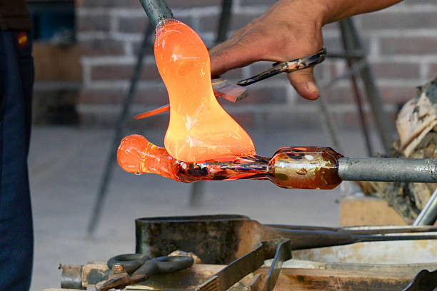 Close up view of skilled craftspeople making a turtle figure out of hot coloured glass.