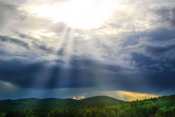 Rays of sun from behind clouds over forest and mountains after rain