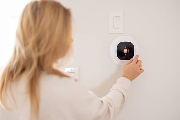 istock Woman Adjusting Smart Thermostat on Wall for Comfortable Room Temperature 2208181720