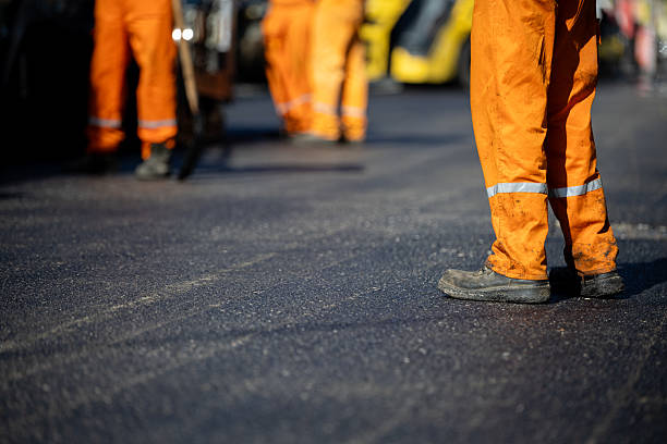 istock Construction workers in orange uniforms laying asphalt on a busy road during daylight hours 2208183455