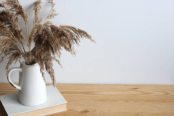 istock Pampas grass in white jug resting on book on wooden table in the boho style 2208184375
