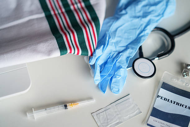 Various medical tools including gloves, a stethoscope, a syringe, and identification card are neatly displayed on a white table, representing healthcare preparation and organization.