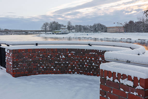 A snow-covered brick parapet with a railing on the river bank at dawn. High quality photo