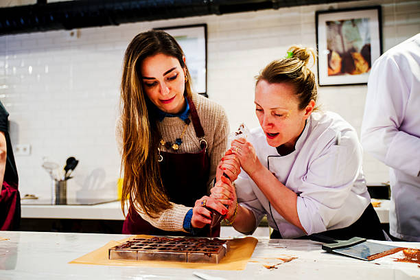 A cook uses a chocolate bag to fill shapes for chocolate desserts during a pastry chocolate making class. Close-up of a dessert master pouring a container for the dessert mass to solidify