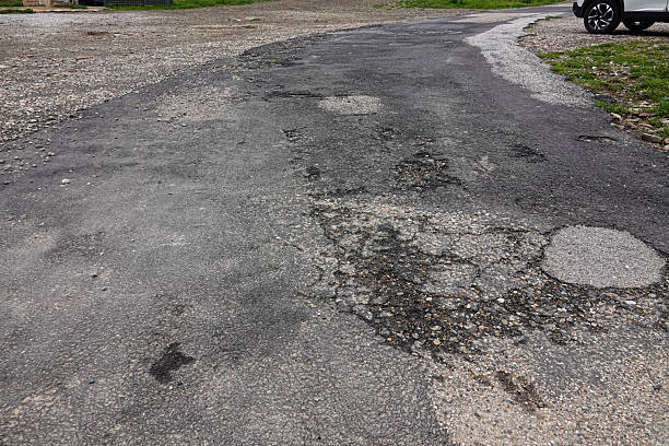 istock A cracked and uneven road stretches through a suburban landscape, displaying various potholes and patches. 2208201219