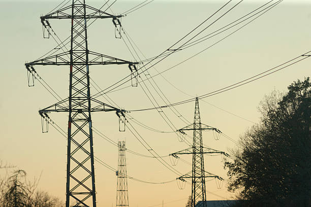 The power lines and tall transmission towers are beautifully silhouetted against a stunning sunset background