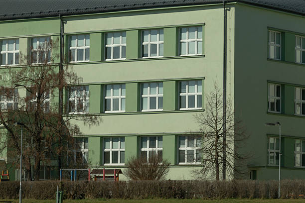 Green School Building with Large Windows and Trees in Background