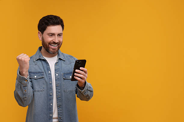 istock Happy man with smartphone on orange background. Space for text 2208209118