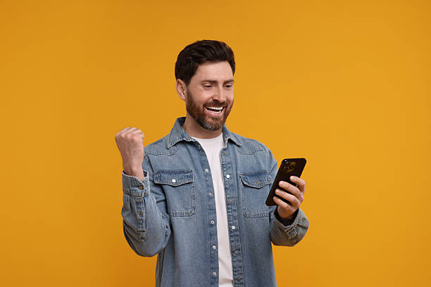 istock Happy man with smartphone on orange background 2208209349