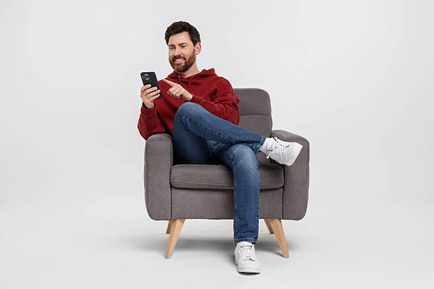 istock Happy man with smartphone sitting on armchair against white background 2208209457