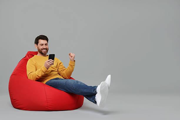 istock Happy man with smartphone sitting on bean bag against grey background. Space for text 2208209458