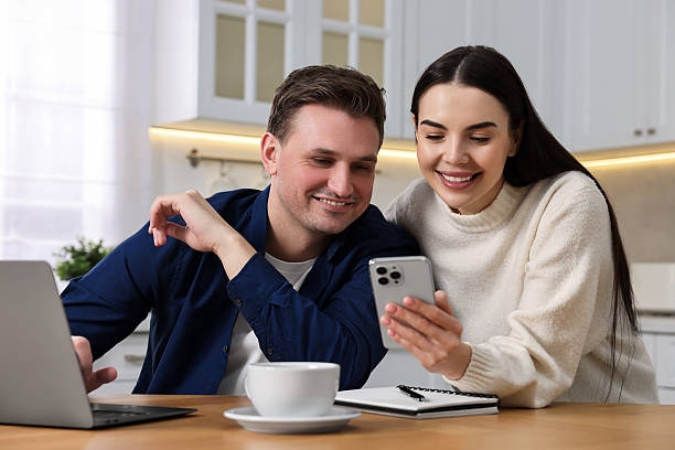 istock Happy couple using gadgets together at wooden table in kitchen 2208210729