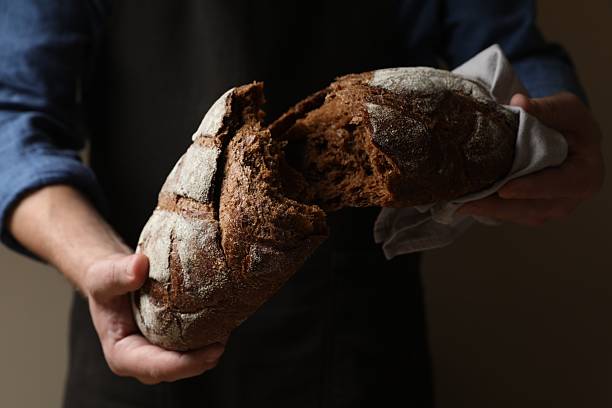 istock Man breaking loaf of fresh bread on dark background, closeup 2208213808