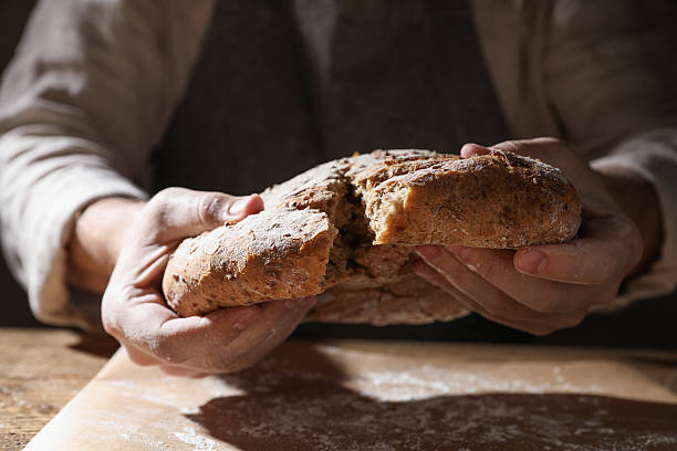 Man breaking loaf of fresh bread at wooden table, closeup