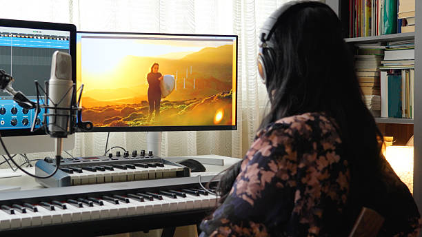 Woman with headphones records voice over movie using microphone in front of computer screens with AI in music composition software in modern home music studio.