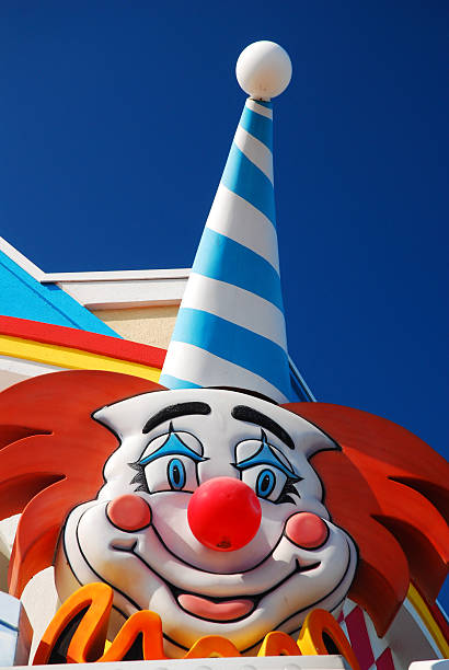 A creepy clown dressed in a large hat with flowers on it.