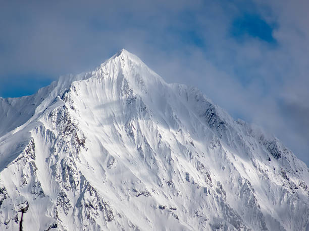 A snow-covered mountain peak at Kootenay National Park with dramatic ridges and slopes, under a partly cloudy sky