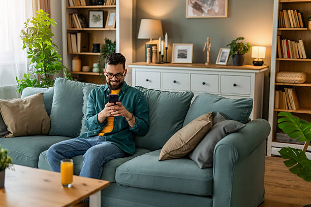 istock Happy young man using smart phone while relaxing on sofa at home. 2208233731