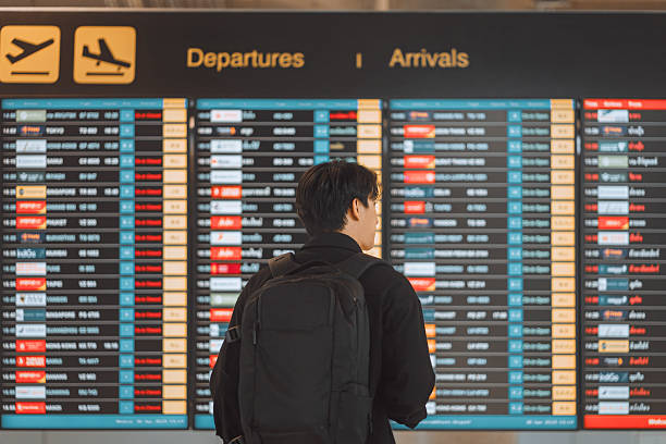 istock Young asian man with backpack and suitcase walking through airport terminal and checking flight at departure information, Traveling by airplane 2208241647