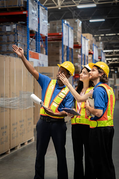 istock Three workers in safety vests are looking at a stack of boxes. They are pointing at the boxes and discussing something 2208243020