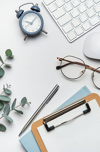 istock Workspace organizing eucalyptus branches, keyboard, mouse, alarm clock, clipboard, pen, and eyeglasses on white table 2208244313