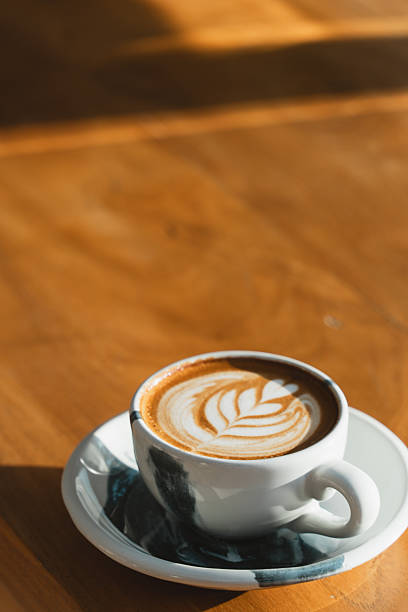 istock A ceramic cup with latte art on a wooden table, illuminated by sunlight. 2208248533