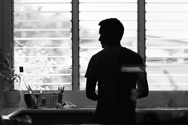 istock Thoughtful young man in the kitchen home alone looking out window. 2208248724