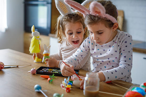 Two cute girls painting eggs for Easter holiday in kitchen