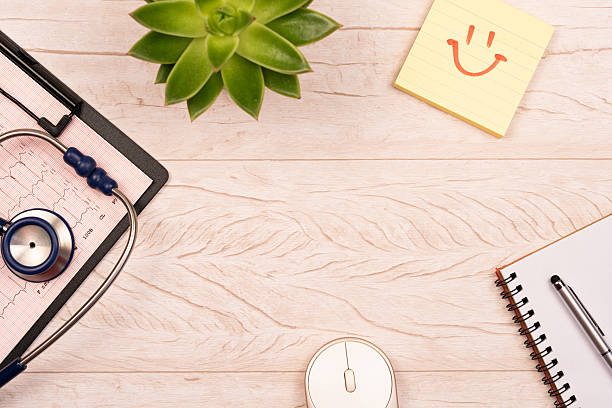 Medical workspace with stethoscope, clipboard, hands clasped, symbolizing compassionate professional healthcare environment from overhead perspective