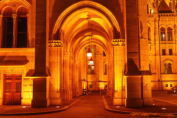 Budapest, Hungary - November 24, 2024: Warmly lit archway leads into the Hungarian Parliament Building, showcasing intricate architectural details in Budapest during nighttime.