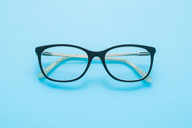 istock Eyeglasses with dark black plastic frame on light blue table background. Pastel color. Closeup. Top down view. 2208267538