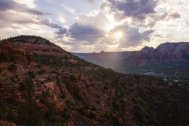 Scenic view of Sedona's red rock formations under a dramatic sky with sun rays breaking through clouds.
