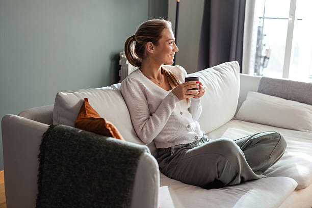 istock A young woman relaxing on her couch while enjoying a warm beverage 2208272063
